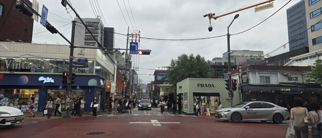 성수동 팝업 상권이 들어선 성수이로 사거리 전경, 왼쪽에 만원 균일가 빈티지 매장과 인형뽑기 가게, 오른쪽에 프라다 임시 구조물 매장이 마주 보고 있다