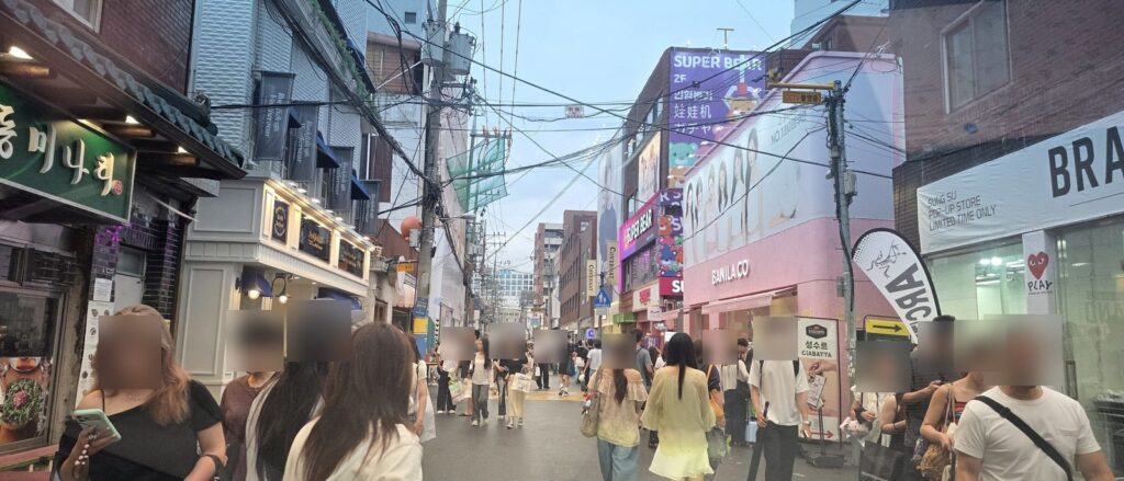 성수동 연무장길 거리 전경, 팝업스토어 배너와 브랜드 매장들이 늘어서 있고 왼쪽 끝에 기와 처마가 보인다